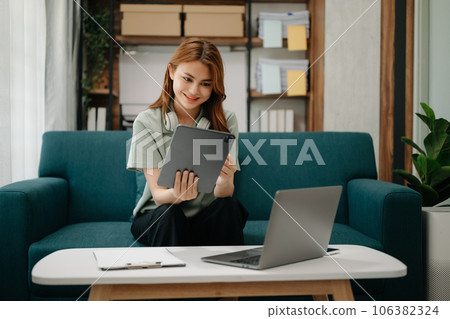 Business woman using tablet and laptop for doing math finance, tax, report, accounting, statistics, and analytical research concept on sofa in home office. 106382324