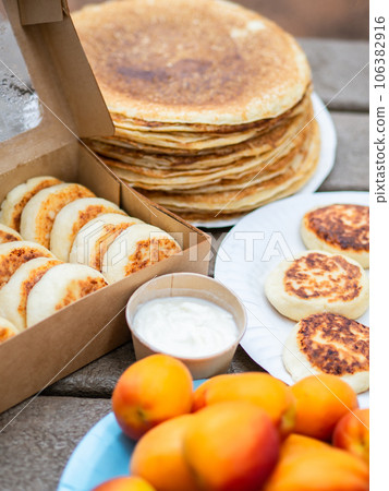 Cottage cheese pancakes, syrniki in paper box and stack thin pancakes on wood table. Cottage cheese pancakes, syrniki in paper box and stack thin pancakes on wood table. 106382916