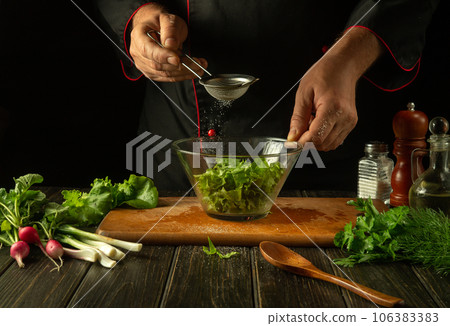 The chef peppers chopped lettuce leaves in a bowl. Working environment in a restaurant kitchen. Delicious salad with fresh vegetables 106383383