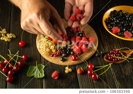 Many different fresh berries on the kitchen table. Man's hands sorting raspberries before preparing fruit drink or compote Many different fresh berries on the kitchen table. Man's hands sorting raspberries before preparing fruit drink or compote 106383398