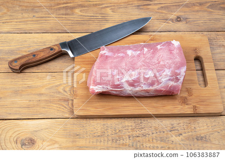 Raw pork meat on a cutting board and a kitchen knife. 106383887