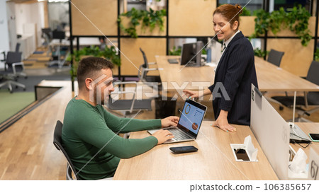 Red-haired caucasian woman and bearded man standing at the desktop. Colleagues discussing work. Red-haired caucasian woman and bearded man standing at the desktop. Colleagues discussing work. 106385657