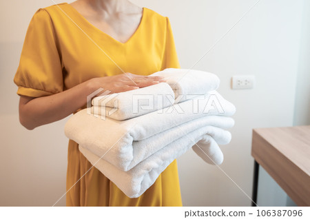 Cropped shot of hotel maid holding the stack of towels in hotel bedroom. Conceptual of female chambermaid making bed in hotel room. Cropped shot of hotel maid holding the stack of towels in hotel bedroom. Conceptual of female chambermaid making bed in hotel room. 106387096