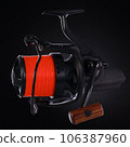 Black fishing reel with orange fishing line, on a black background. Close-up 106387960