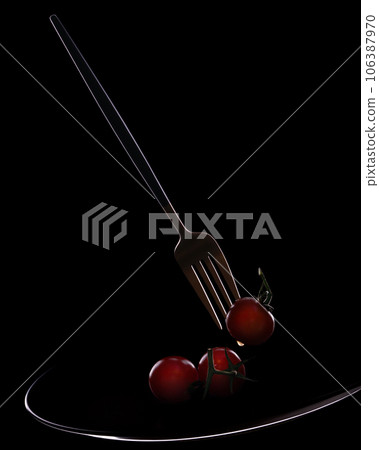 Fork with small tomatoes on a black background, on a plate. Fork with small tomatoes on a black background, on a plate. 106387970