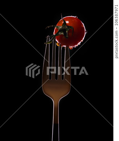 Fork with small tomatoes on a black background Fork with small tomatoes on a black background 106387971