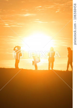 Travelers silhouettes against the orange light of sunset on the mountains. 106388458