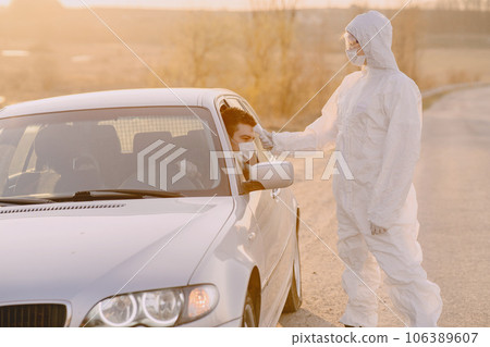 Person in a protective suit. Doctor checks the temperature in the berson behind the whell. 106389607