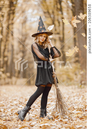 Blonde young girl witch in forest on Halloween. Girl wearing black dress and cone hat. Witch holding a broom. 106389658