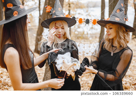 Three young girls witches in forest on Halloween. Girls wearing in black dresses and cone hat. Witch holding a magician stuff. Three young girls witches in forest on Halloween. Girls wearing in black dresses and cone hat. Witch holding a magician stuff. 106389660
