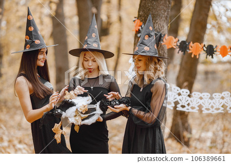 Three young girls witches in forest on Halloween. Girls wearing black dresses and cone hat. Witch holding a magician cauldron. Three young girls witches in forest on Halloween. Girls wearing black dresses and cone hat. Witch holding a magician cauldron. 106389661