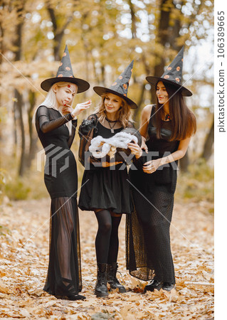 Three young girls witches in forest on Halloween. Girls wearing black dresses and cone hat. Witches holding a magician cauldron. Three young girls witches in forest on Halloween. Girls wearing black dresses and cone hat. Witches holding a magician cauldron. 106389665