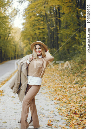 Woman posing for a photo in the autumn park. Caucasian girl has red lips. Woman wearing beige coat and a hat. Woman posing for a photo in the autumn park. Caucasian girl has red lips. Woman wearing beige coat and a hat. 106389691