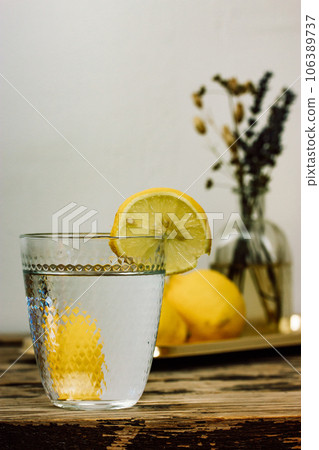 Still life with homemade lemonade made of fresh lemons on a wooden rustic table. Beautiful composition with a cut glass with clear water and a vase with field flowers. Infused water with lemon slice. 106389737