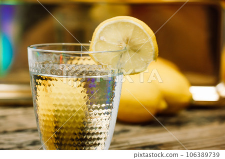Still life with homemade lemonade made of fresh lemons on a wooden rustic table. Beautiful composition with a cut glass with clear water and a vase with field flowers. Infused water with lemon slice. 106389739