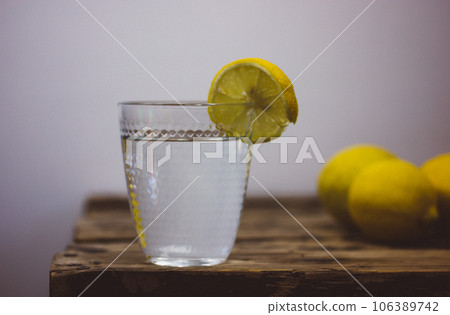 Still life with homemade lemonade made of fresh lemons on a wooden rustic table. Beautiful composition with a cut glass with clear water and a vase with field flowers. Infused water with lemon slice. 106389742