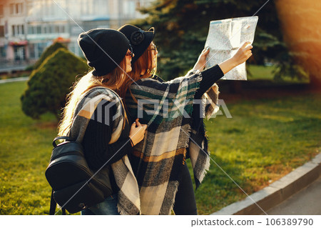 Two young stylish girls travel in an unknown city with a map Two young stylish girls travel in an unknown city with a map 106389790