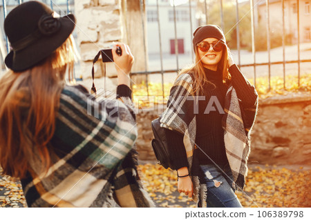 Two young stylish girls photograph each other on a camera in a sunny city 106389798