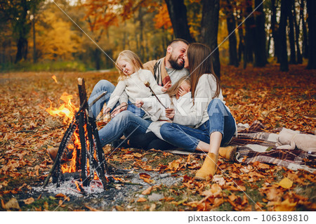 Family in a autumn park. Woman in a red sweater. Cute childrens with parents sitting near fireplace Family in a autumn park. Woman in a red sweater. Cute childrens with parents sitting near fireplace 106389810