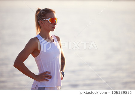Portrait of active woman runner in sport clothes and sunglasses on seashore. Woman relaxing, resting after morning fitness routine. 106389855