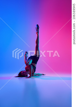Young beautiful flexible woman dancer on high heels posing on floor in contemporary dance style, pole dance in colorful gradient neon light. Young beautiful flexible woman dancer on high heels posing on floor in contemporary dance style, pole dance in colorful gradient neon light. 106389945