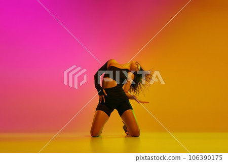 Front view portrait of young flexible girl dancing on knees on floor over background in neon with mixed lights. Front view portrait of young flexible girl dancing on knees on floor over background in neon with mixed lights. 106390175