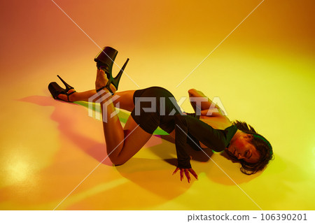 Top view portrait of young beautiful fit woman dancer posing on floor in the style of synch wave in colorful neon light. Top view portrait of young beautiful fit woman dancer posing on floor in the style of synch wave in colorful neon light. 106390201