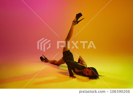 Young beautiful fit woman heels dance posing on floor in the style of synch wave in colorful gradient neon light. 106390208