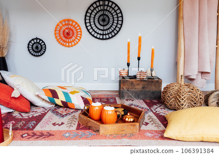 Decorated cozy autumn interior for relax during fall holidays. Comfy floor location with cushions, wicker pumpkins, burning candles. Thanksgiving, Halloween plans at home. Romantic date, movie night. 106391384