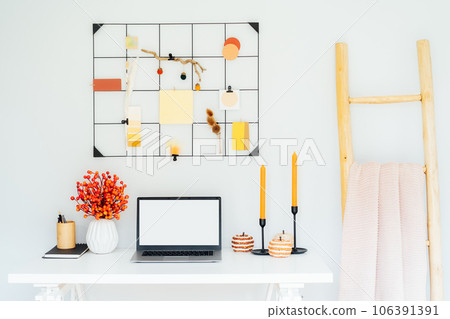 Home office desk with open laptop mockup, grid mood board with fall colors palette and seasonal decor like candles, flowers, pumpkins, plaid. Autumn inspiration and cozy mood. Hygge home fall decor 106391391