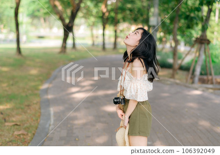 Portrait of asian young woman traveler with weaving hat and basket and a camera on green public park nature background. Journey trip lifestyle, world travel explorer or Asia summer tourism concept. Portrait of asian young woman traveler with weaving hat and basket and a camera on green public park nature background. Journey trip lifestyle, world travel explorer or Asia summer tourism concept. 106392049