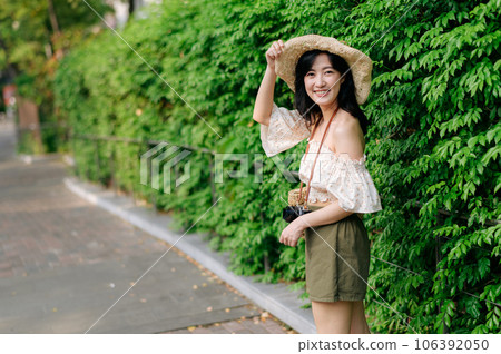 Portrait of asian young woman traveler with weaving hat and basket and a camera on green public park nature background. Journey trip lifestyle, world travel explorer or Asia summer tourism concept. Portrait of asian young woman traveler with weaving hat and basket and a camera on green public park nature background. Journey trip lifestyle, world travel explorer or Asia summer tourism concept. 106392050