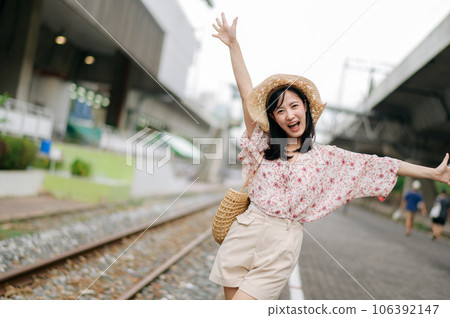 young asian woman traveler with weaving basket happy smiling looking to a camera beside train railway. Journey trip lifestyle, world travel explorer or Asia summer tourism concept. young asian woman traveler with weaving basket happy smiling looking to a camera beside train railway. Journey trip lifestyle, world travel explorer or Asia summer tourism concept. 106392147
