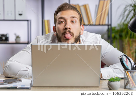 Office businessman hiding behind laptop computer making funny silly face fooling around, disrespect Office businessman hiding behind laptop computer making funny silly face fooling around, disrespect 106392268