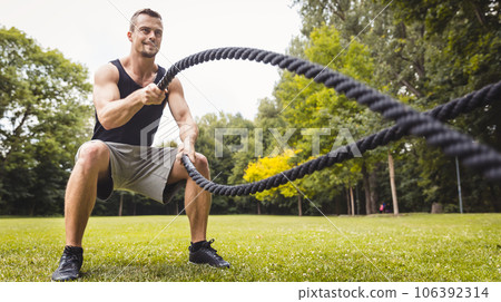 Man in park using battle rope 106392314