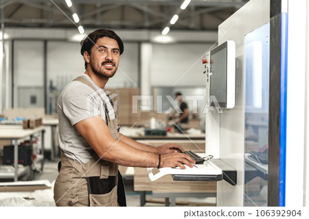 Young carpenter operating machine for wood processing at a furniture factory 106392904