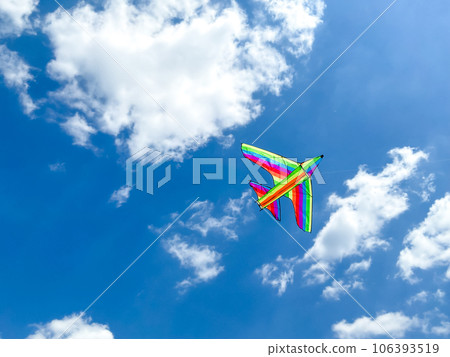 Multicolored kite flies in the blue sky on a sunny day. Empty space for an inscription. Multicolored kite in the form of an airplane. Multicolored kite flies in the blue sky on a sunny day. Empty space for an inscription. Multicolored kite in the form of an airplane. 106393519