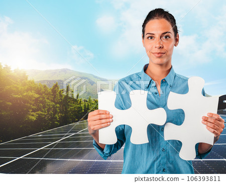Woman holds two pieces of puzzle over a roof with solar panels 106393811