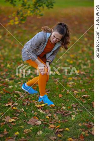 sad elegant woman in fitness clothes in park having leg pain 106396759