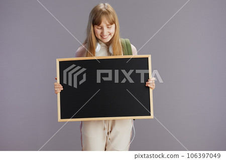 happy trendy pupil in beige tracksuit showing blank board 106397049