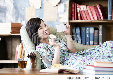 一位女士一邊吃糖果一邊用智能手機看電影 一位女士一邊吃糖果一邊用智能手機看電影 106398925