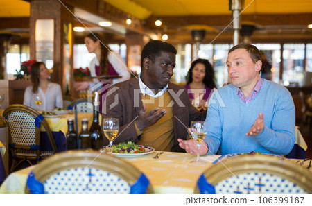Two male friends sitting at table in restaurant and talking 106399187