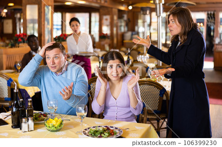 Resentful wife scolding her husband spending time with another woman at dinner Resentful wife scolding her husband spending time with another woman at dinner 106399230