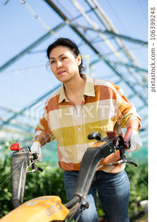 Female horticulturist using walking tractor in hothouse 106399248