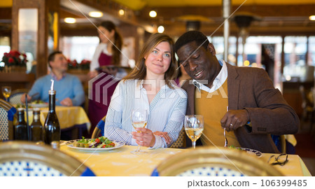 Cheerful adult biracial couple enjoying dinner in restaurant Cheerful adult biracial couple enjoying dinner in restaurant 106399485