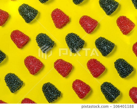 Background of red and black chewy candies in the form of berries on a yellow background. Sweets in the form of raspberries . Marmalade isolate. Sliced candy for kids. 106401188