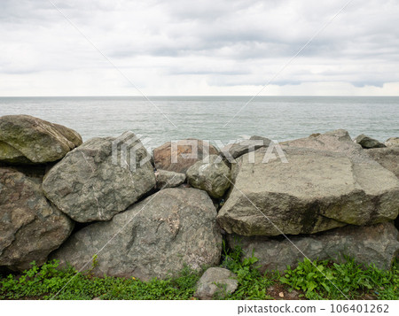 Barrier of large stones on the seashore. Wave protection. Irregular stones. Sea shore. Barrier of large stones on the seashore. Wave protection. Irregular stones. Sea shore. 106401262
