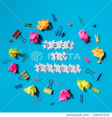 BACK TO SCHOOL message inscription text on white puzzles on creative colorful blue background around stationery supplies. Educational greeting announcement for students and teacher. Top view flat lay 106402918