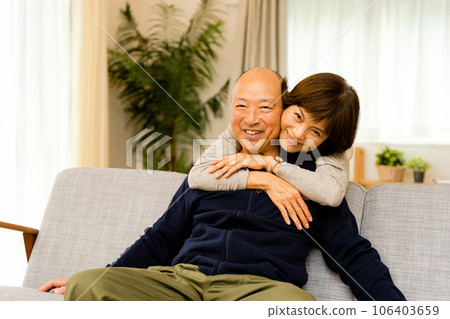 A wife hugging her husband sitting on the sofa from behind (an affectionate expression of a senior couple) A wife hugging her husband sitting on the sofa from behind (an affectionate expression of a senior couple) 106403659
