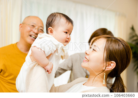 A smiling mother holding a 0-year-old baby and a grandfather watching 106403660